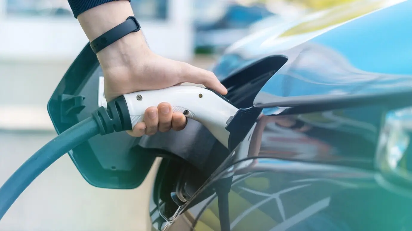 A man plugs a charger into an electric car at a charging station.